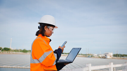 An engineer dressed in safety gear focuses on a laptop while using a smartphone at a solar power...