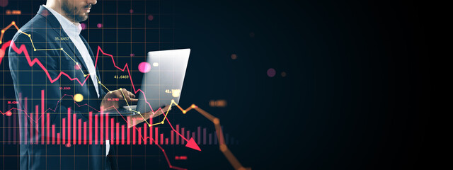 Businessman analyzing financial market crash using laptop with red downward graph and charts on dark background indicating global crisis.