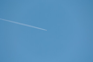 aereo di linea che vola in alto nel cielo azzurro e sereno, di giorno, visto dal basso e da lontano, mentre lascia dietro di se la scia di condensazione