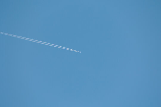 aereo di linea che vola in alto nel cielo azzurro e sereno, di giorno, visto dal basso e da lontano, mentre lascia dietro di se la scia di condensazione