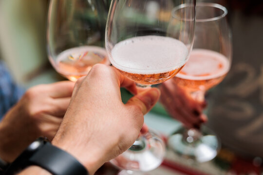 dettaglio sulle mani di tre persone adulte, all'interno di una stanza, che fanno un brindisi con dei calici riempiti con bevande diverse, per festeggiare 