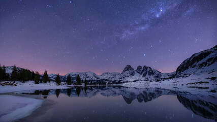 Crystal-clear lake reflecting snowy mountains under starry night sky, long exposure style