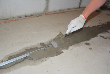 The builder covers the aluminum beacons with cement mortar for subsequent pouring of the floor with concrete.