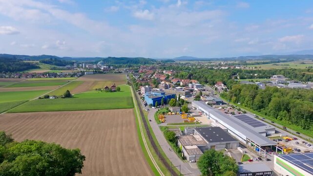 Aerial view of the town nestled amid lush green fields and buildings, a contrast of rural and urban textures under a clear sky, Aarberg, Canton of Bern, Switzerland.