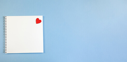 Spring-loaded notebook with square white sheets and a red heart on a blue background. Notebook Blank for Notes, Space for Copy, Text and Advertising, Banner, School Notebook, Business, Blank Sheet