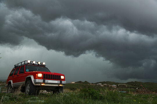 Sevan, Armenia - May 12, 2013 - 1996 red modified, lifted, stock old 4x4 Jeep Cherokee XJ Country 4.0L off-road SUV vehicle with roof rack military lights, MT tires, in mountains at thunderstorm  
