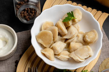 Closeup of homemade dumplings pelmeni with greenery and pepper, served in rustic plate on dark wooden background.