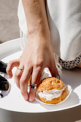 Woman’s hand taking choux pastry with cream filling from white plate, minimal elegant dessert scene, airy low calorie sweet concept.