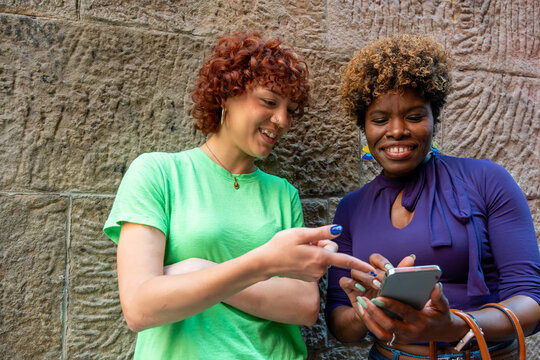 Two young women using smartphone against stone wall