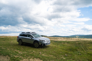 Silver SUV on Grassy Hill with Cloudy Sky