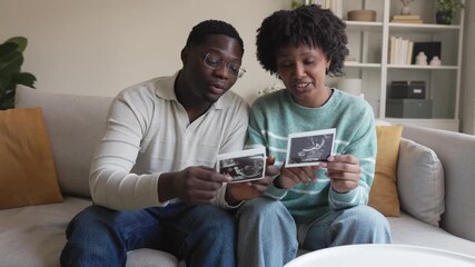 Happy black couple examining ultrasound scan photos on sofa - Powered by Adobe
