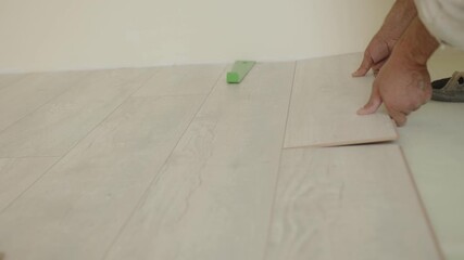 A worker carefully lays down laminate flooring in a residential space, ensuring precise placement. The light enhances the wood-like texture and color of the planks, creating a fresh atmosphere.