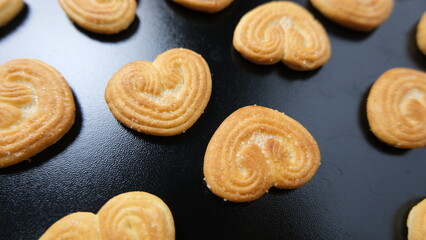 Golden brown palmier cookies arranged on a sleek black background, highlighting their heart shape and flaky layered texture.
