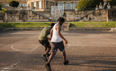 Two teen guys playing street basketball on old urban court at sunset