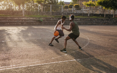 Teen boys playing intense urban basketball game on outdoor court at sunset