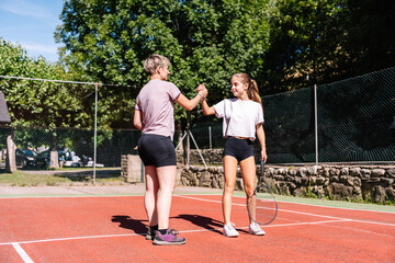 Two women athletes shaking hands after playing tennis match on a sunny day, celebrating victory and fair play