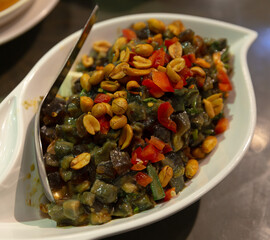 Spicy century egg salad with diced red peppers, crushed peanuts, and herbs served in a white ceramic dish with metal spoon