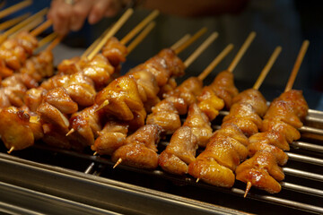 Grilled chicken tails skewered and cooked over flame at a night market stall, with glistening golden skin and savory caramelization
