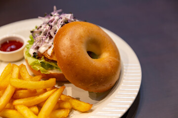 Top-down view of bagel sandwich topped with lettuce and microgreens, served with golden French fries and ketchup on a white ceramic plate