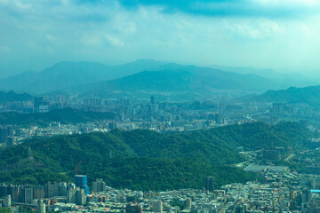 Obraz premium Panoramic view of Taipei City with distant mountains, showing a blend of dense urban structures and lush green hills under hazy blue skies