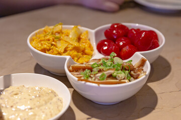 Assorted Taiwanese side dishes in a divided serving bowl, including marinated pig ear slices with scallions, candied cherry tomatoes, and spicy cabbage