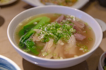 Chinese clear broth noodle soup with tender beef brisket and beef tendon, garnished with green onions and bok choy in a white bowl