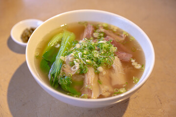 Traditional Chinese beef noodle soup with sliced brisket and tendon in clear broth, served with bok choy and chopped scallions