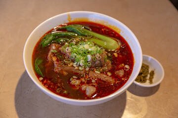 Spicy Sichuan-style noodle soup with beef brisket and beef tendon in red chili oil broth, topped with scallions and served with bok choy