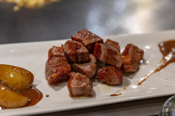 Close-up of juicy seared beef steak cubes served with roasted potatoes and brown sauce on a white plate, showcasing Japanese teppanyaki cuisine