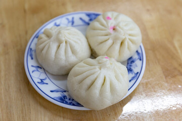 Top view of three traditional Chinese steamed buns neatly arranged on a decorative white and blue floral plate over a wooden tabletop