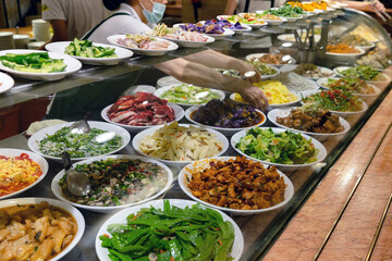 Variety of Taiwanese dishes displayed at a buffet-style self-service counter, with plates full of vegetables, meats, and stir-fried options behind glass