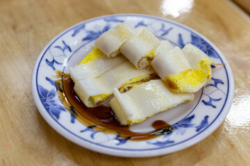Egg pancake slices made from rice flour crepe, served with thick soy paste, presented on a traditional blue floral plate over wooden table