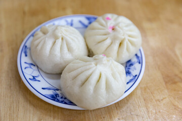 Close-up of traditional Chinese baozi on a patterned plate, focusing on soft pleated dough and...
