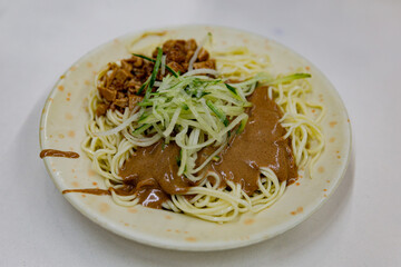 Cold sesame noodle dish topped with shredded cucumber, minced pork sauce, and rich sesame paste, served on a round ceramic plate