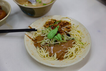 Close-up of Taiwanese cold noodles with sesame paste, minced pork, shredded vegetables, and a small dollop of wasabi on top, served on ceramic plate