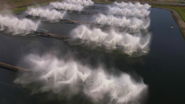 Rows of nozzles spray water into cooling basins at Minsk TPP 5 near Minsk, Belarus. Continuous motion creates mist above the ponds amid nearby vegetation.