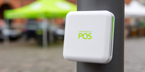 White square device with "POS" text is attached to a pole, blurred background. Concept: contactless, technology, outdoor