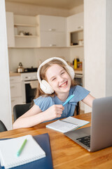 Smiling girl with headphones studying online on laptop, engaged in e-learning at home