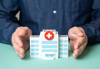 Obraz na płótnie Canvas A man protects a hospital building with his hands. Concept of protecting the healthcare system. Medical security, patient safety, public health protection