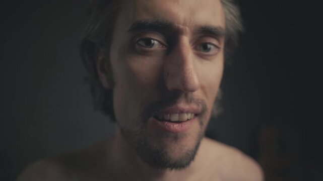 Humorous Close-Up of a Reflective Man Shifting from Seriousness to a Playful Smile in Dim Lighting