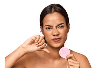 Woman holds facial sponge in studio showing a dislike gesture, thumbs down. Disagreement concept.