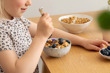 The girl has granola with yogurt and berries for breakfast on the table. 