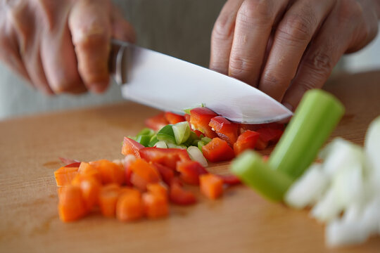 Close-up of hands chopping fresh red bell pepper and celery on a cutting board