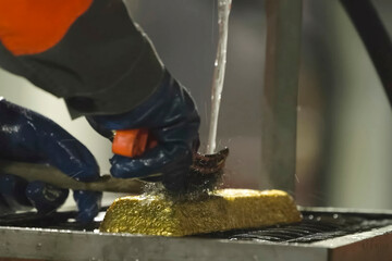 Washing and cleaning with metal brush of a gold bar after smelting.