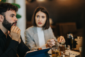 Two colleagues engage in a focused conversation during an informal meeting in a relaxed cafe setting. They discuss ideas while enjoying a casual, creative atmosphere over beverages.