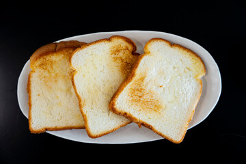 Toasted Bread Slices on Plate: Three slices of toast, golden brown edges, on a white plate with a black background.