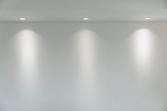 Modern room interior with recessed lighting illuminating a minimalist white wall, creating a bright space.