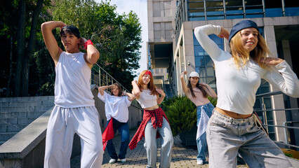 Street dance group performing synchronized choreography outdoors with joyful energy. Concept of youth culture, lifestyle, dance schools, fashion creativity and modern social promotion.