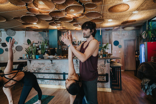 Instructor assisting individuals during a yoga session in a comfortable and creatively designed interior, focusing on movement, balance, and wellness.