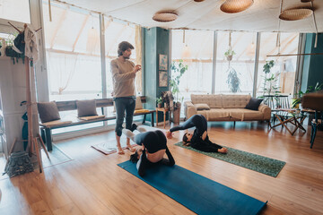 A yoga instructor observes participants while they practice challenging yoga postures on mats in a well-decorated and serene studio space.
